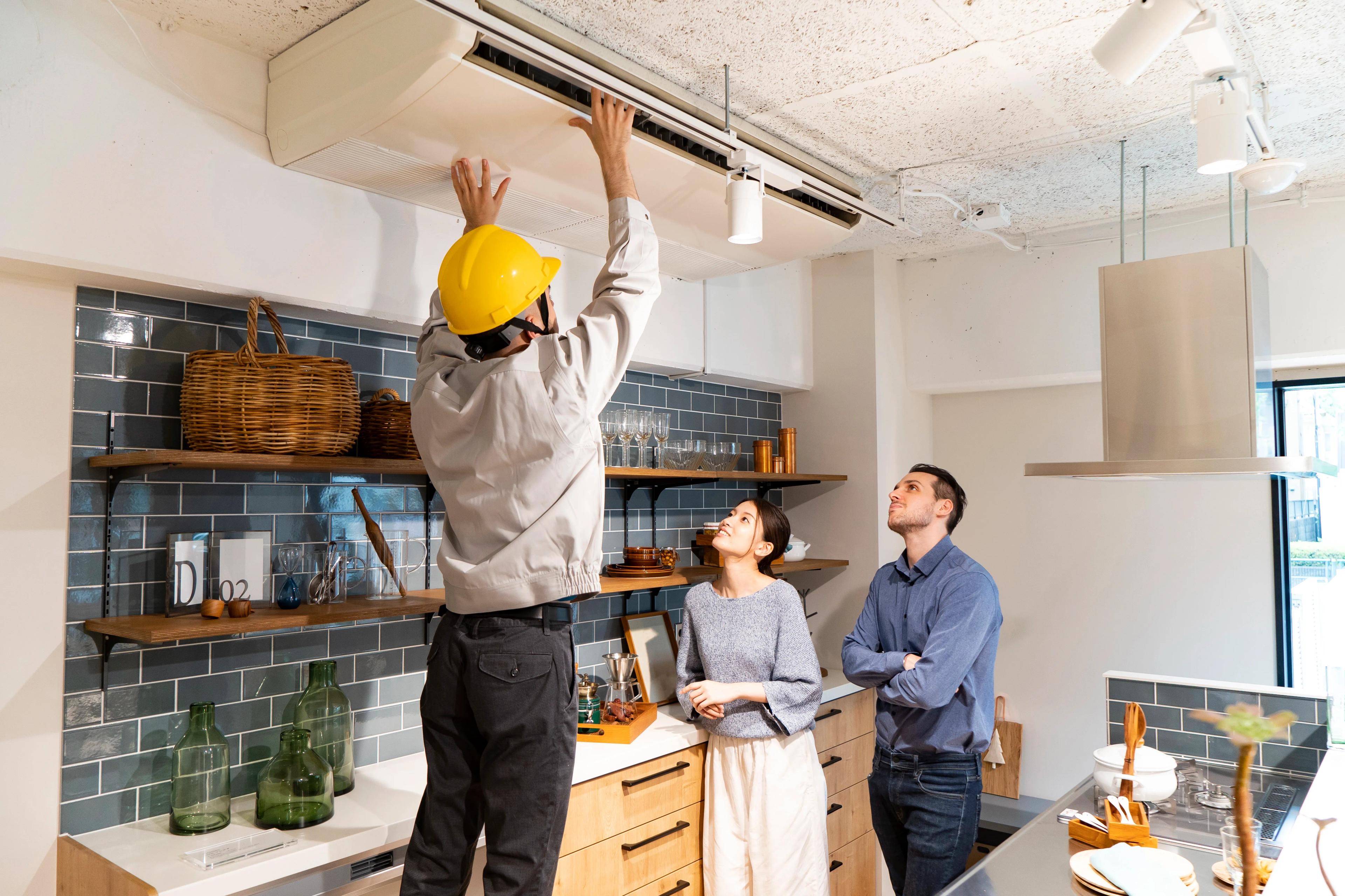 contractor with yellow hard hat installing a PKA indoor unit in the kitchen with onlooking homeowners standing nearby