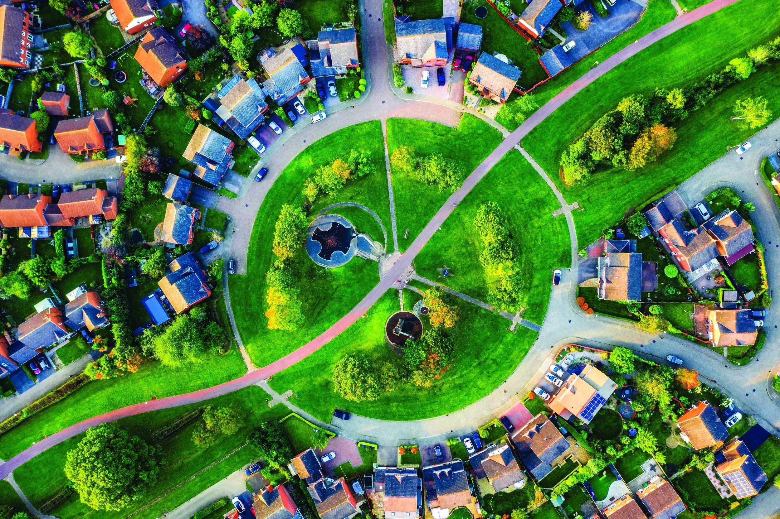 overhead aerial shot of green park with trees and walking paths surrounded by homes