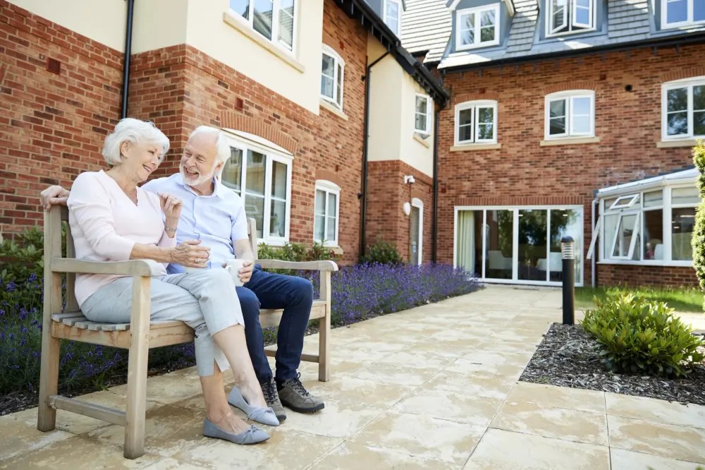 mature senior couple sitting on bench smiling outside senior living facility